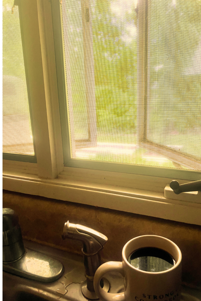 Open window with coffee cup siting on sink ledge