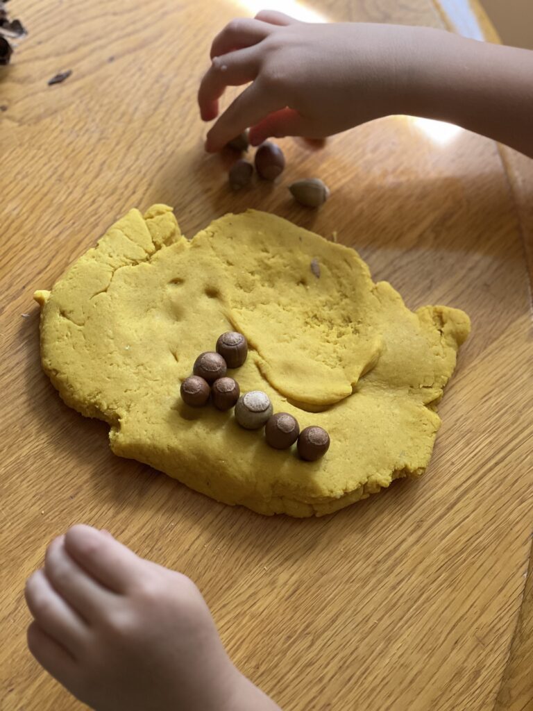 child adding acorns to yellow playdough